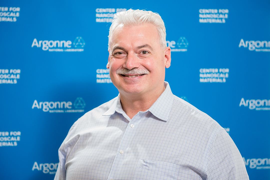 Smiling man in front of Blue Argonne logo backdrop.