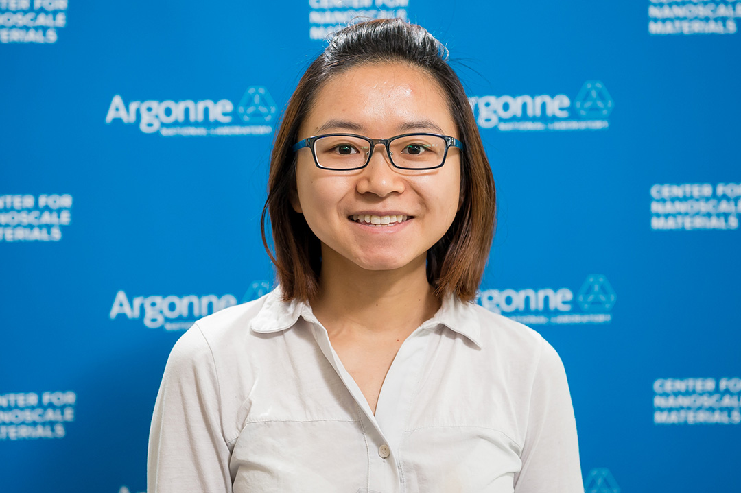 Smiling woman wearing glasses, in front of Blue Argonne logo backdrop.