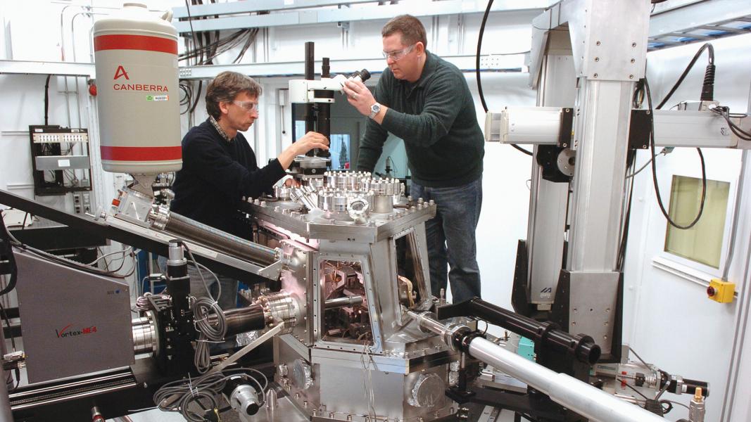 Two men wearing safety goggles working on microscopes.