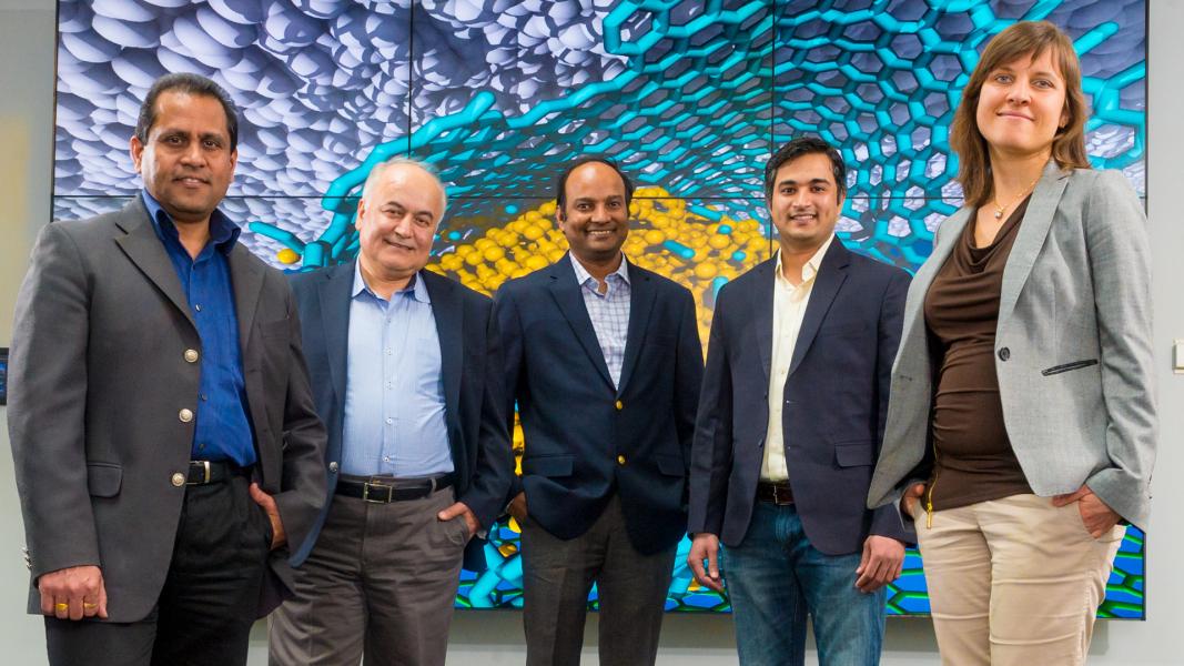 Five smiling people in front of colorful wall mural.