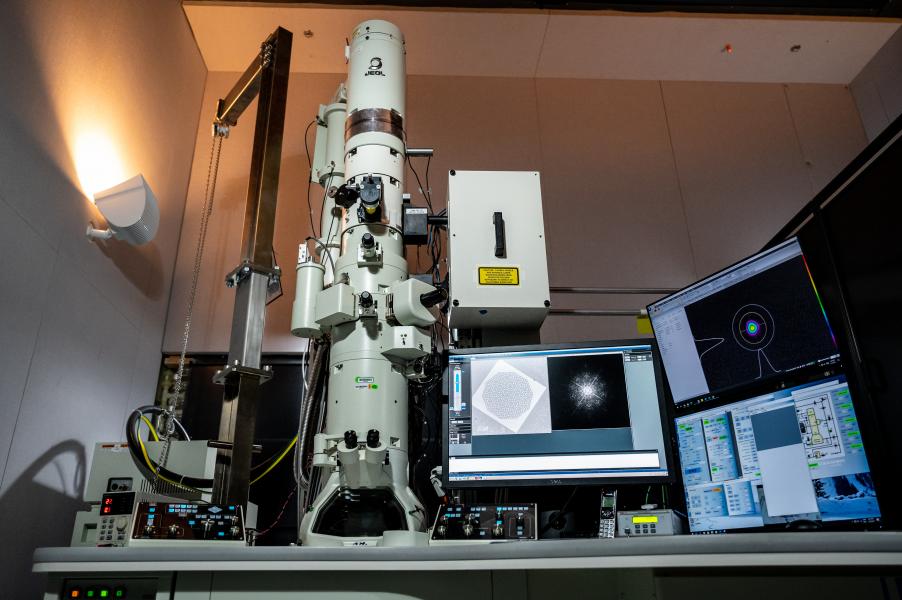 View looking upwards at microscope that towers over desk with multiple computer monitors.